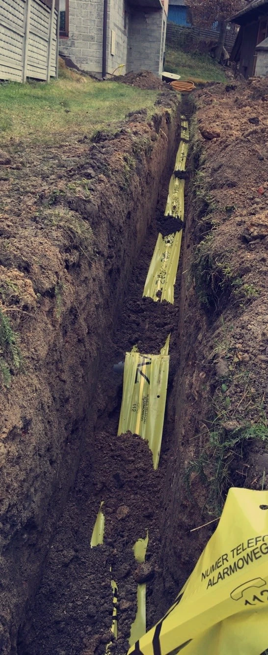 Rów wykopany w ziemi z ułożonymi żółtymi osłonami ochronnymi dla podziemnych przewodów